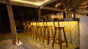 A row of wooden chairs with a patterned tile wall behind them, under a thatched roof structure. - Aldea Coba an Escape Resort (Coba)