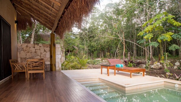 A wooden deck with a stone wall, a thatched roof, and a pool area with a bench and lounge chair. - Aldea Coba an Escape Resort (Coba)
