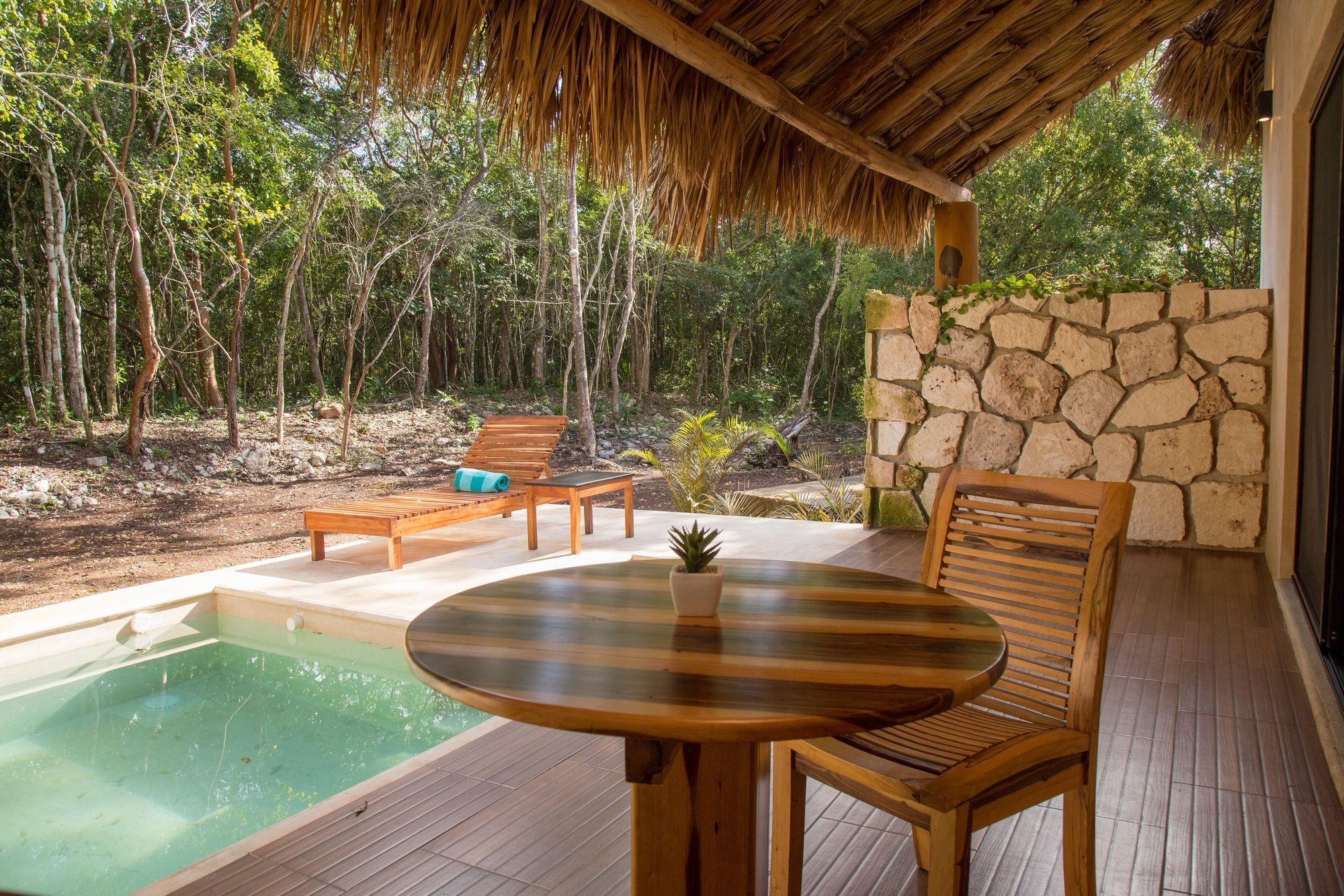 Una terraza de madera con piscina, sillones de descanso y un muro de piedra.