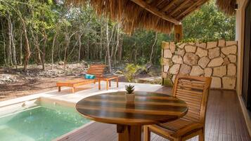 Una terraza de madera con piscina, sillones de descanso y un muro de piedra.