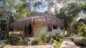 A thatched-roof hut with a stone exterior, surrounded by lush greenery and a paved pathway. - Aldea Coba an Escape Resort (Coba)