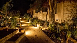 A nighttime pathway leading to stone buildings with thatched roofs, surrounded by tropical plants and illuminated by ground lights. - Aldea Coba an Escape Resort (Coba)