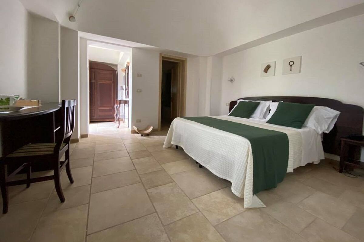 Une chambre à coucher avec un lit, un bureau et une chaise. Une porte donne accès à une autre pièce.
