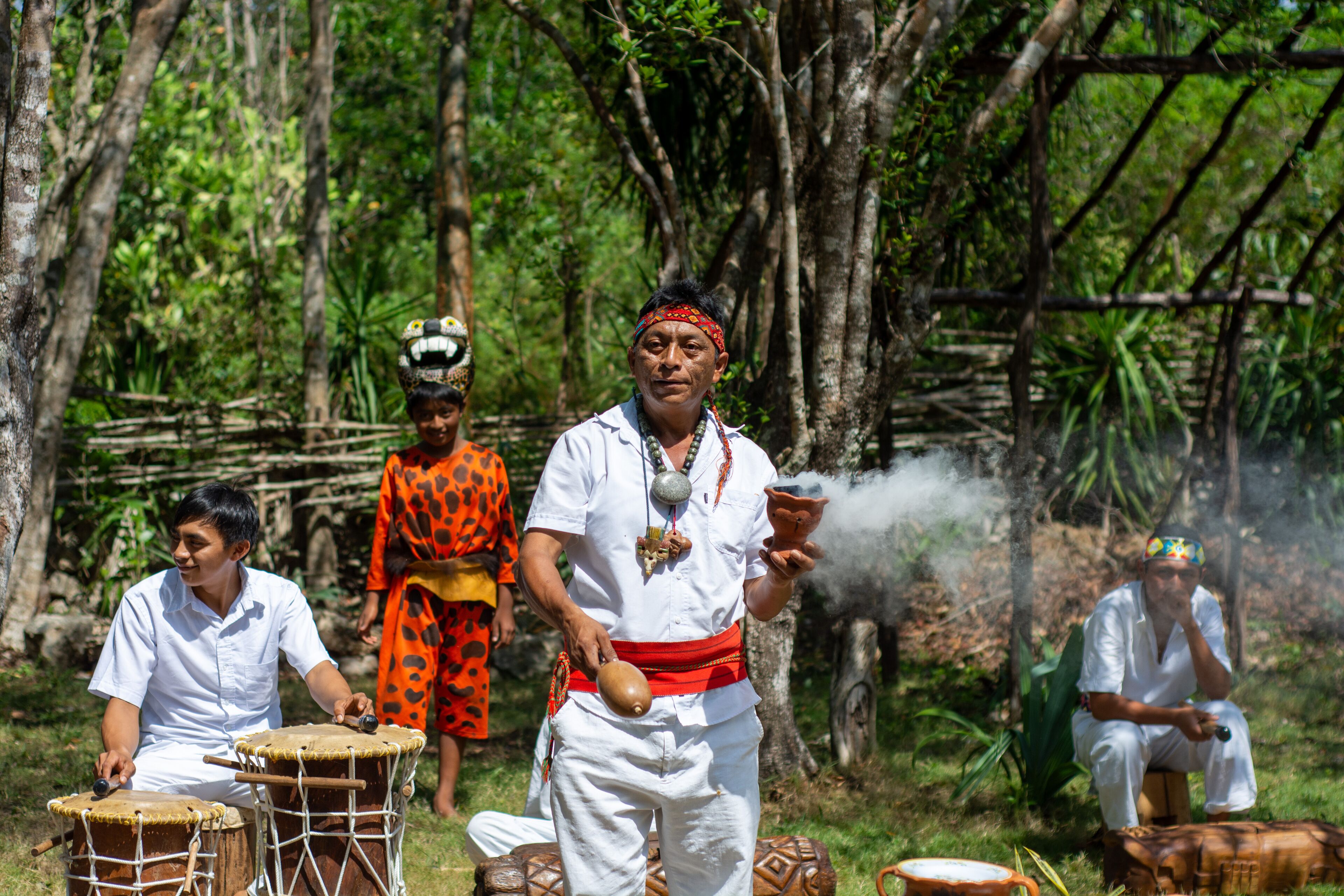 Un grupo de personas vestidas con atuendos tradicionales tocando tambores en un área boscosa.