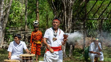 Un grupo de personas vestidas con atuendos tradicionales tocando tambores en un área boscosa.