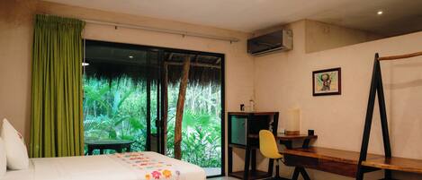A hotel room with two beds, a desk, a chair, and a large window with a view of greenery.
