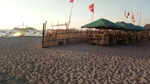 Une plage avec des cabanes à toits de chaume et un bateau traditionnel.