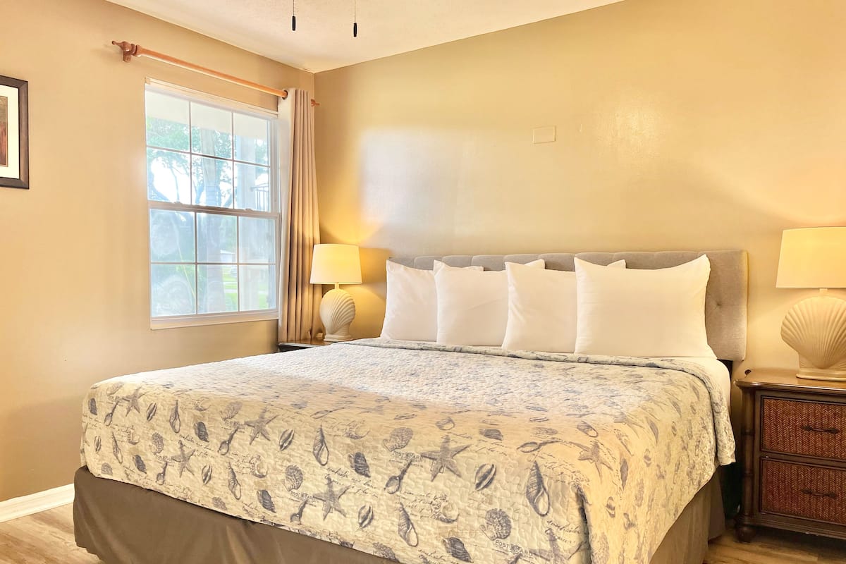 A neatly made bed with a floral-patterned bedspread, a grey upholstered headboard, and white pillows.