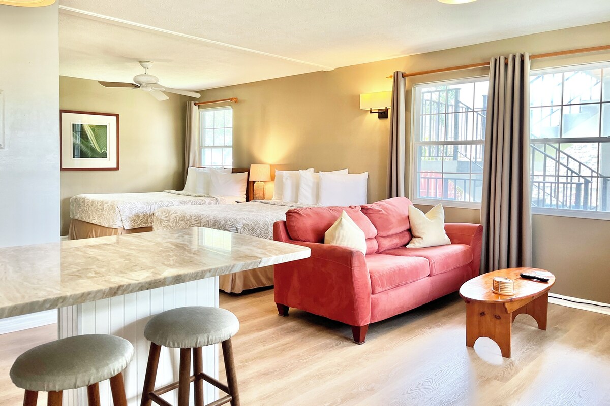 A hotel room with a bed, a red sofa, a small wooden table, and a marble countertop.