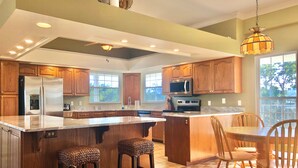 A spacious kitchen with wooden cabinets, stainless steel appliances, a large island with stools, and a dining area with wooden chairs. - Davis House Inn (Sebastian)