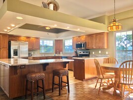 Una cocina amplia con armarios de madera, electrodomésticos de acero inoxidable, una isla grande con taburetes y un comedor con sillas de madera.