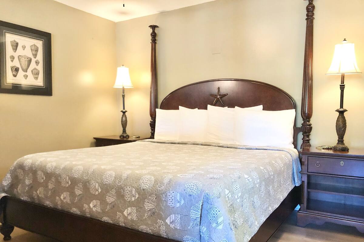 A neatly made bed with a patterned bedspread, two bedside tables with lamps, and a framed picture on the wall.
