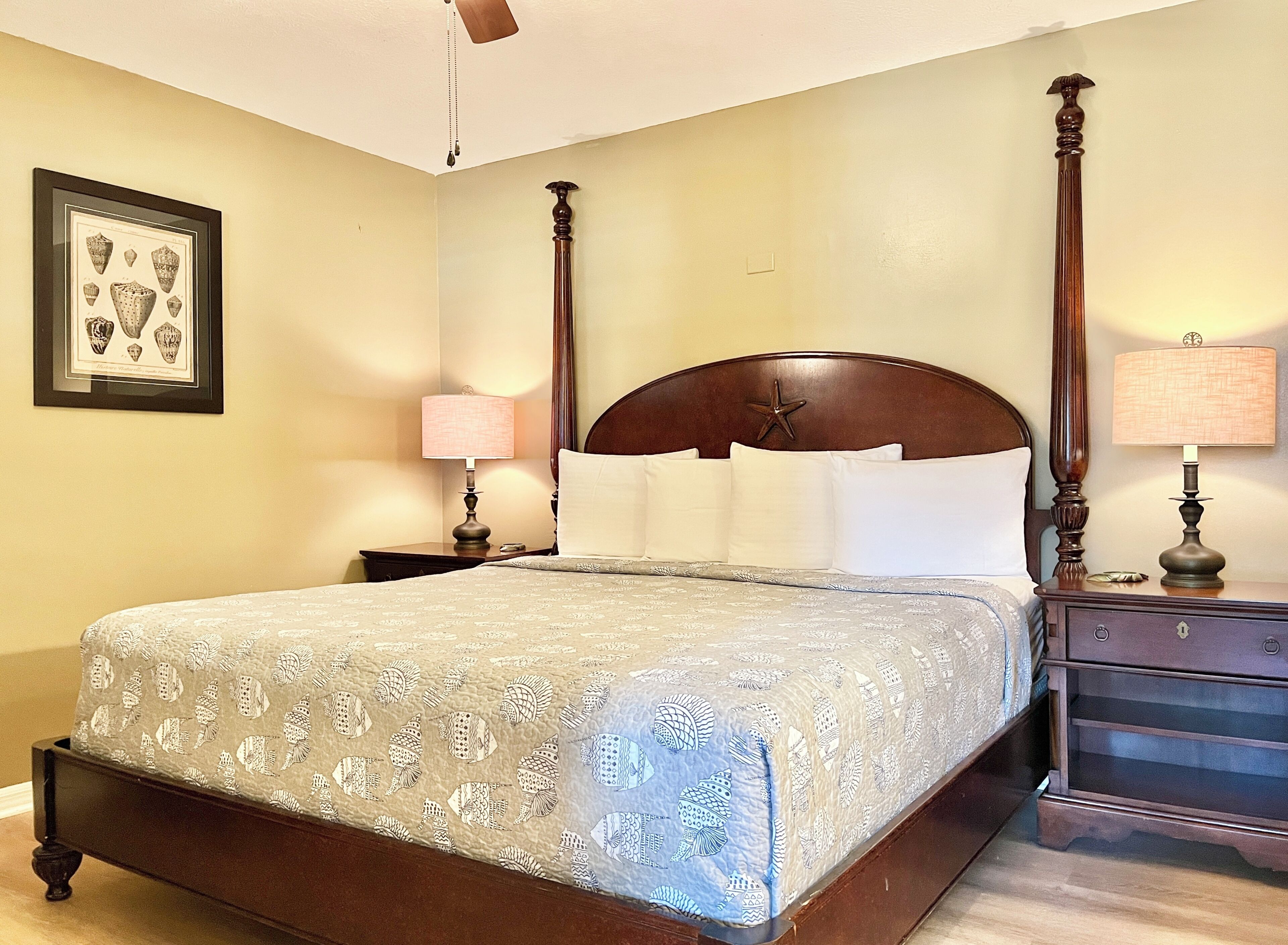 A hotel room with a bed, nightstands, lamps, a ceiling fan, and a framed picture on the wall.