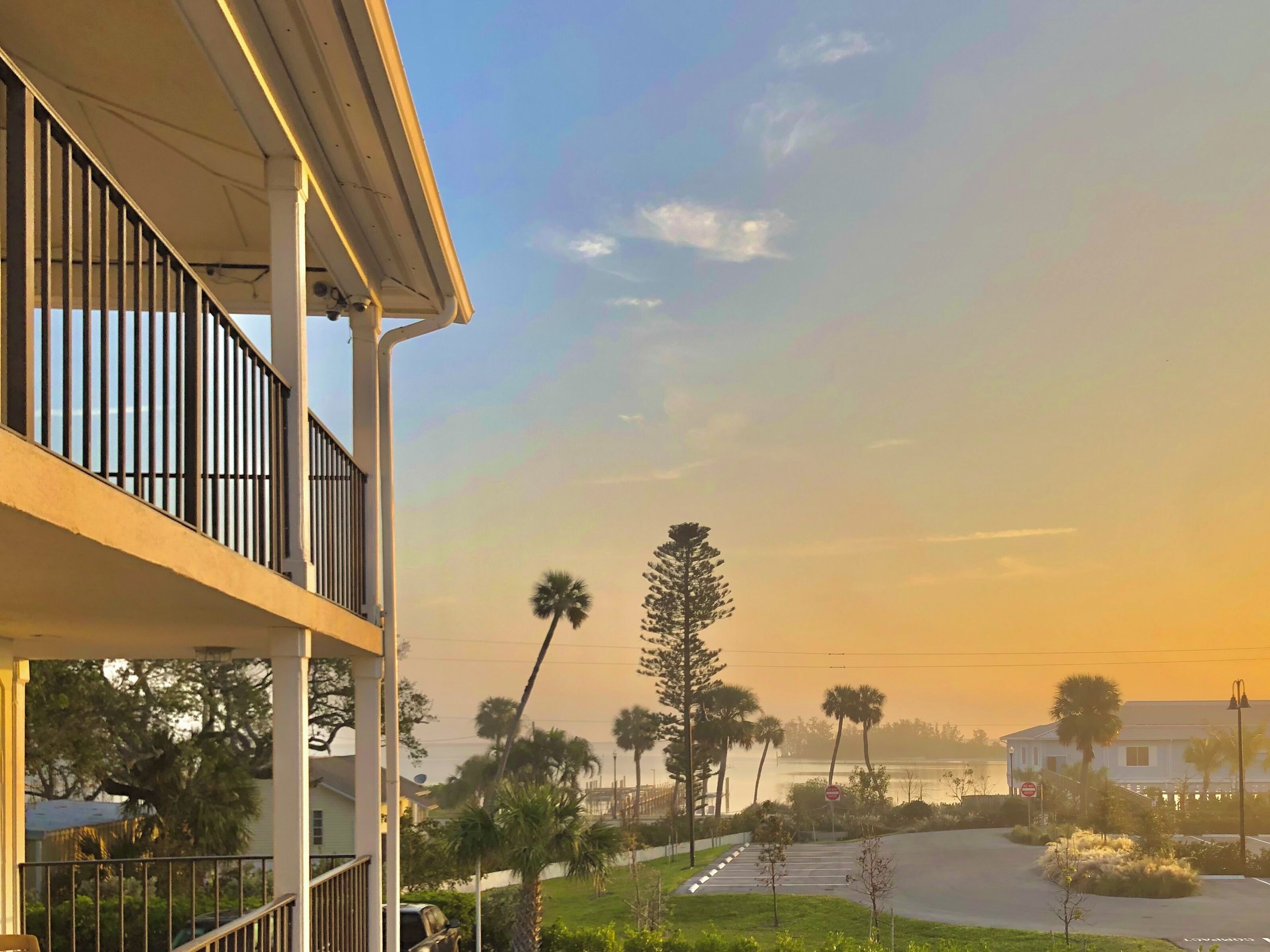 A residential area with a balcony, a street with parked cars, and a body of water in the background.