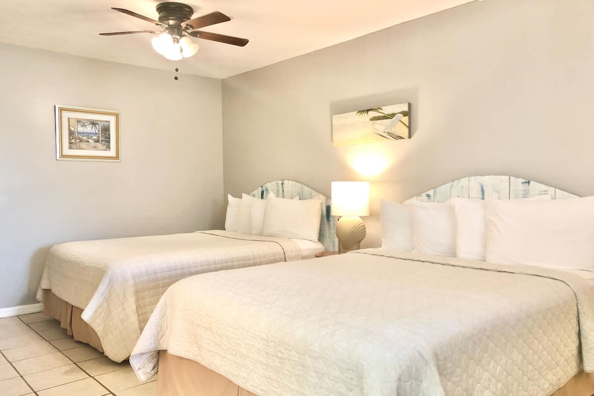 A hotel room with two beds, a ceiling fan, a framed picture on the wall, and a lamp on the nightstand.