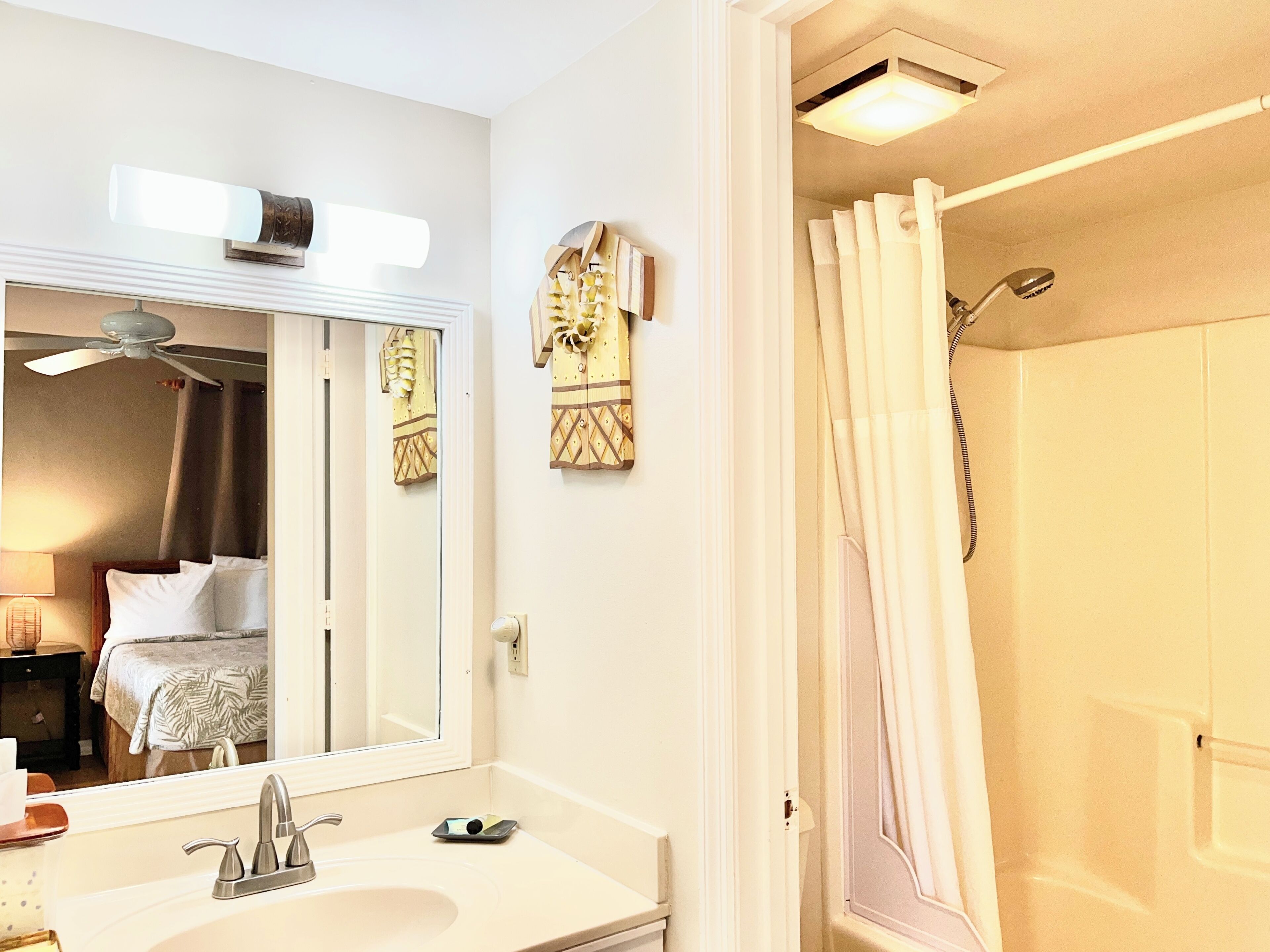 Un baño de hotel con lavamanos, espejo, ventilador de techo y cortina de ducha.