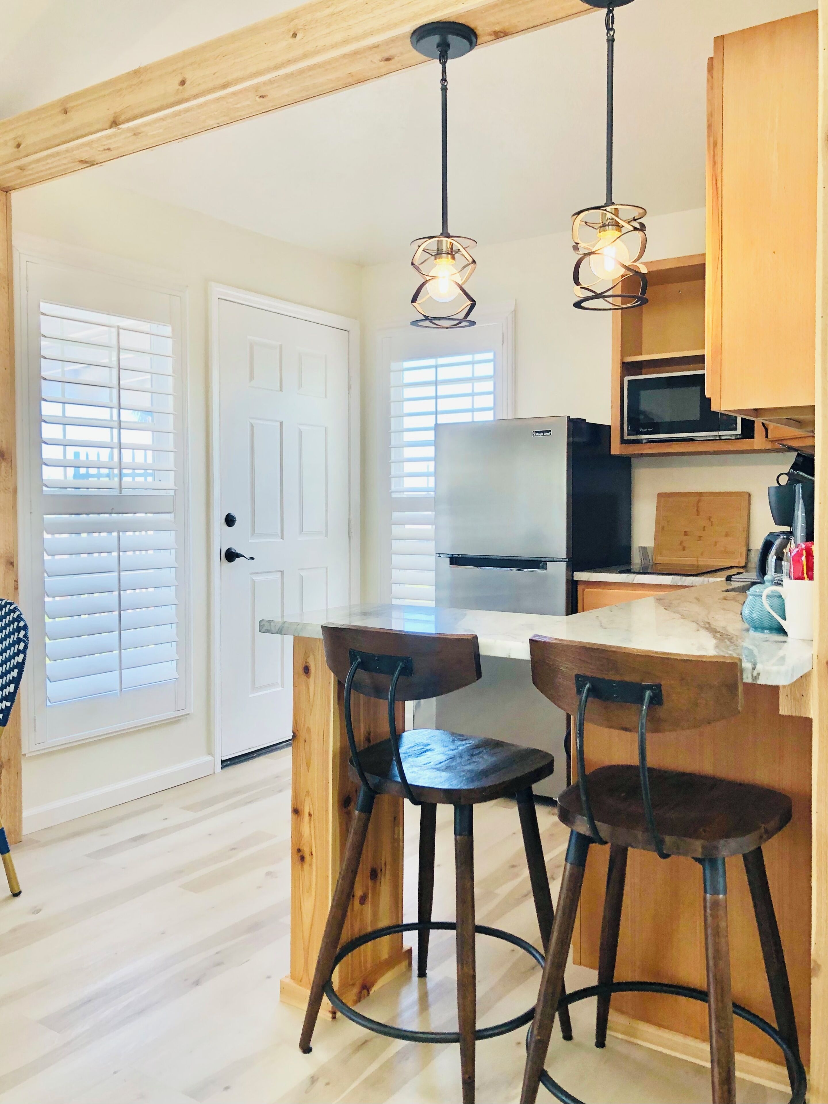 A kitchen with wooden beams, a white refrigerator, a microwave, and two bar stools.
