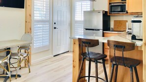 A compact kitchen with a refrigerator, microwave, and bar stools. - Davis House Inn (Sebastian)