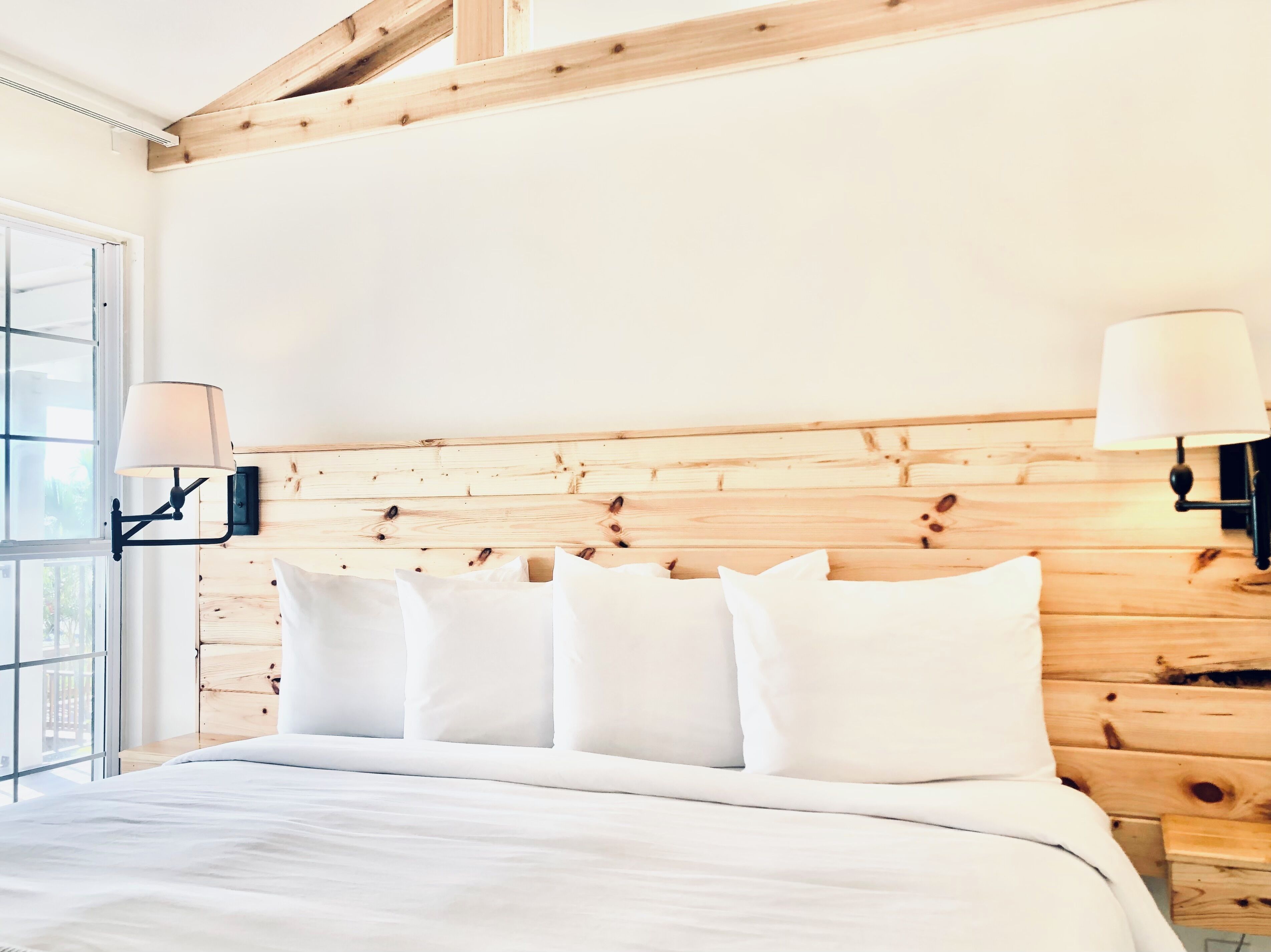 Un dormitorio con cabecera de madera, una cama grande con ropa de cama blanca y dos lámparas fijadas a la pared.