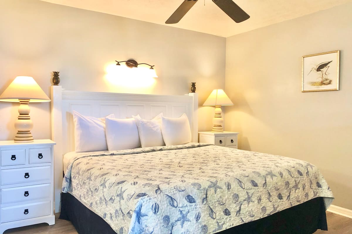 A bedroom with a bed, two bedside tables, a ceiling fan, and wall-mounted lighting.