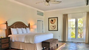 A spacious bedroom with a large bed, a wooden headboard, a nightstand with a lamp, a bench, and a ceiling fan. - Davis House Inn (Sebastian)