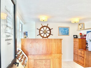 A room with a wooden cabinet, a ship's wheel, and a framed map on the wall.