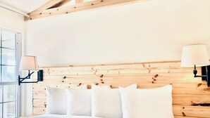 A bedroom with a wooden headboard, white bedding, and two wall-mounted lamps. - Davis House Inn (Sebastian)