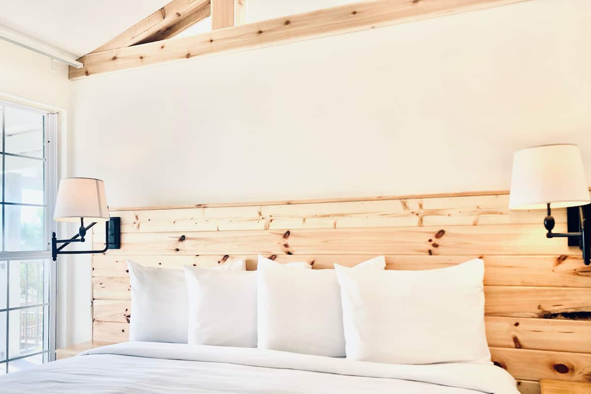 A bedroom with a wooden headboard, white bedding, and two wall-mounted lamps.
