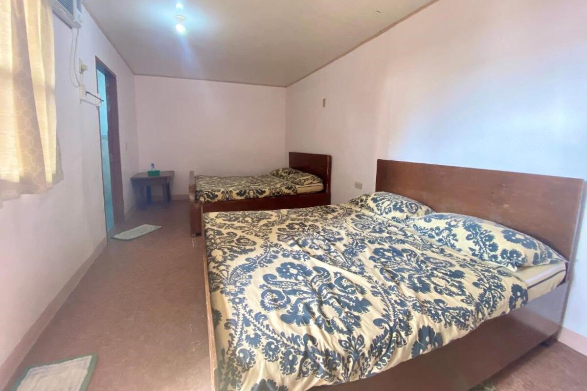 A small, simple room with two single beds, a small table, and a window with curtains.