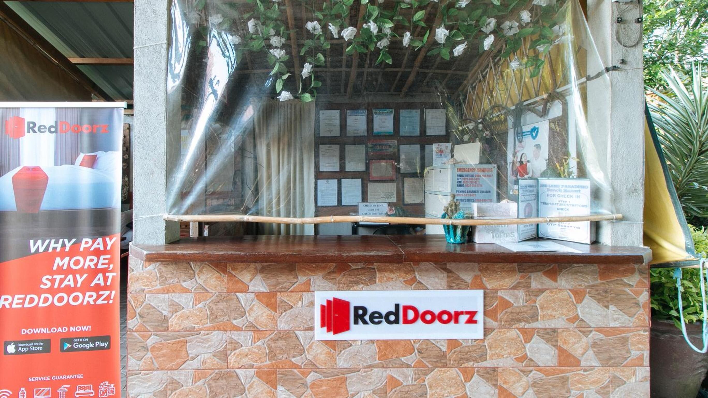 A RedDoorz reception desk with a stone-tiled counter, a sign above it, and a poster advertising the service.