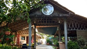 A covered outdoor area with a thatched roof, potted plants, and a pathway leading to a building. - Megan's Paradisio Beach Resort (San Antonio)