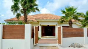 A house with a tiled roof, a wooden fence, and palm trees. - Endless Summer (Noord)