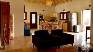 A spacious living area with a high ceiling, a dining table with chairs, and a kitchen in the background. - Endless Summer (Noord)