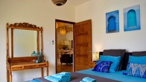 A bedroom with a wooden bed, a bedside table with a mirror, and two blue doors. - Endless Summer (Noord)