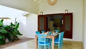 A dining area with a wooden table and blue chairs, a large potted plant, and a ceiling light fixture. - Endless Summer (Noord)