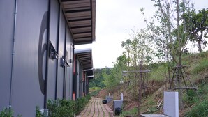 A pathway leading to a building with a modern design, surrounded by greenery and trees. - Phu Sumphao Valley (Phu Ruea)