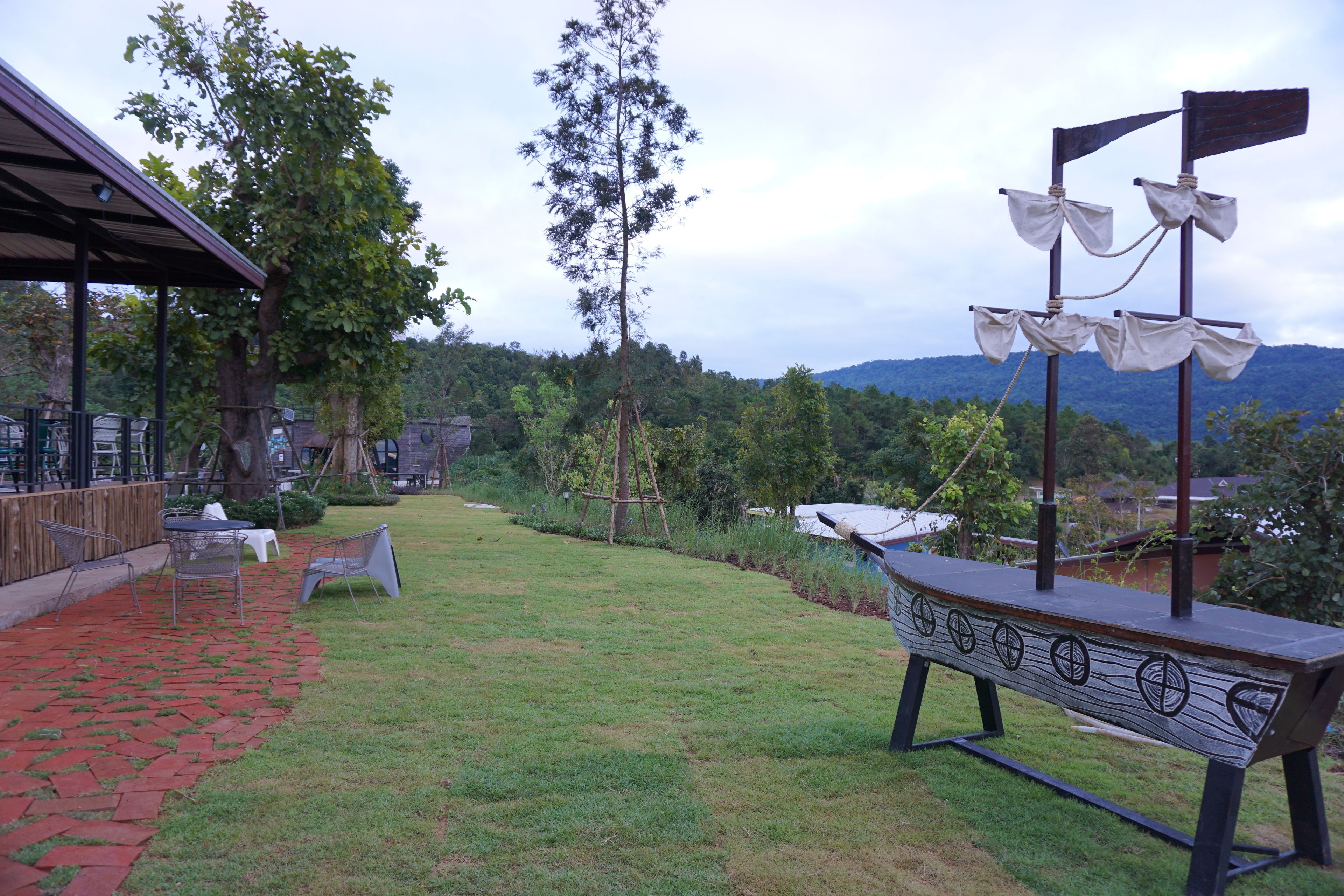 An outdoor seating area with a wooden bench and chairs, a brick pathway, and a view of the surrounding greenery and hills.