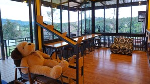A cozy room with a large window, a wooden staircase, and a plush chair. - Phu Sumphao Valley (Phu Ruea)