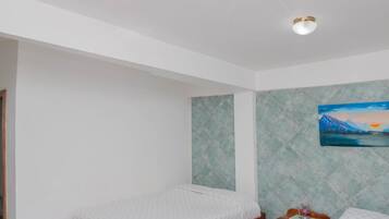Ein Schlafzimmer mit zwei hölzernen Betten, einem kleinen Nachttisch, einem an der Wand hängenden Bild und einem Fliesenboden.