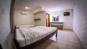A bedroom with a bed, a bedside table, a mirror, and a TV on the wall. - Las Palmas Hotel (Corozal)