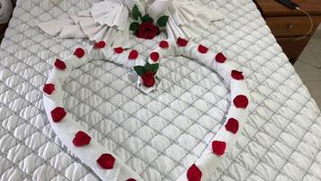 Una cama con una disposición en forma de corazón de toallas blancas y pétalos de rosa roja.