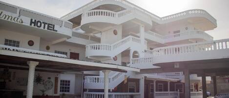 A multi-story hotel with balconies, a central staircase, and a car parked in front.