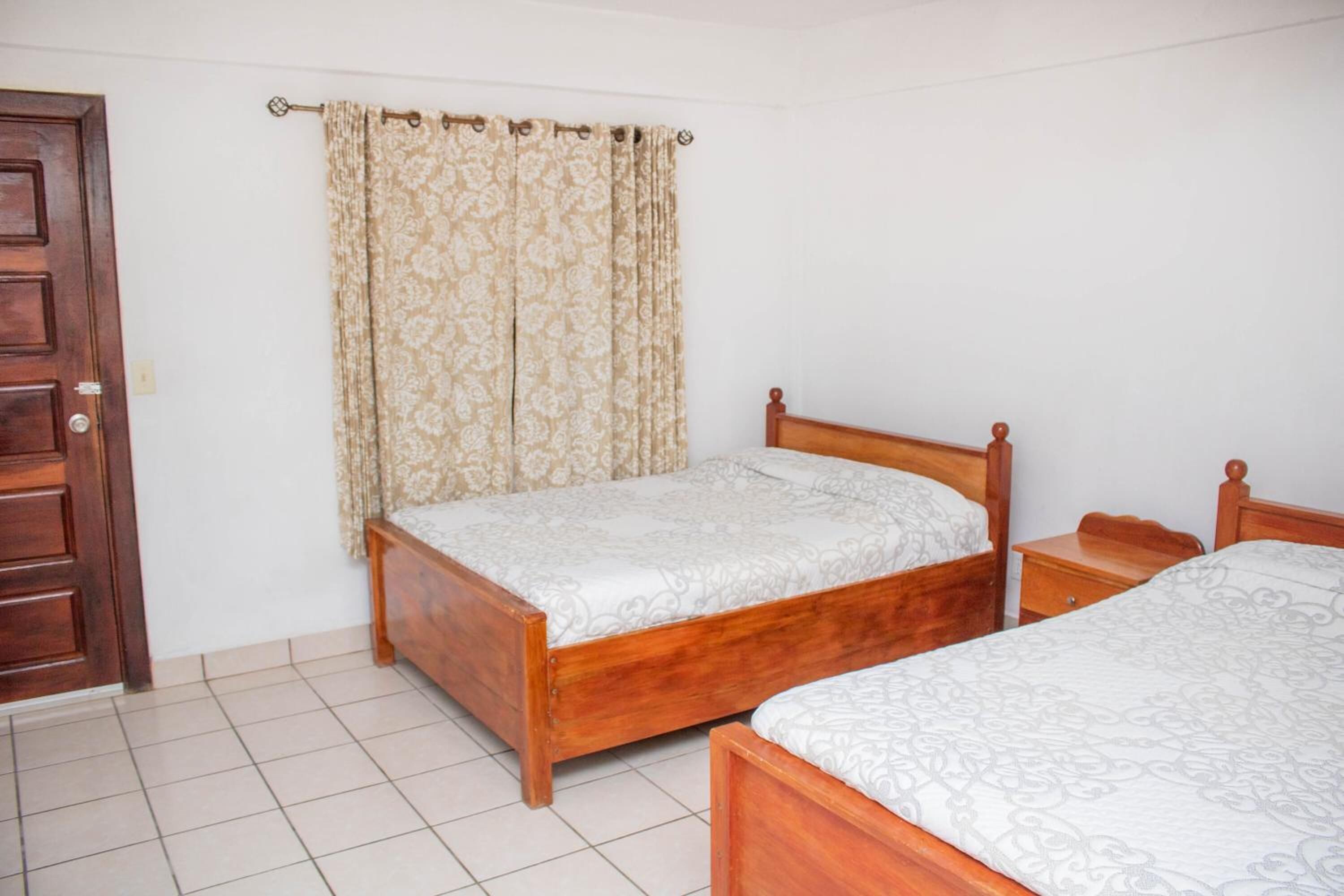 A bedroom with two wooden beds, a wooden nightstand, a wooden door, and a curtain.