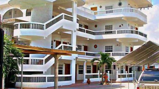 A multi-story building with balconies, a covered entrance, and a parked vehicle. - Las Palmas Hotel (Corozal)