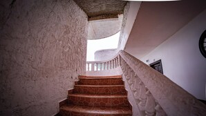 A spiral staircase with stone steps and white balustrades, leading to a landing with a door marked "27". - Las Palmas Hotel (Corozal)