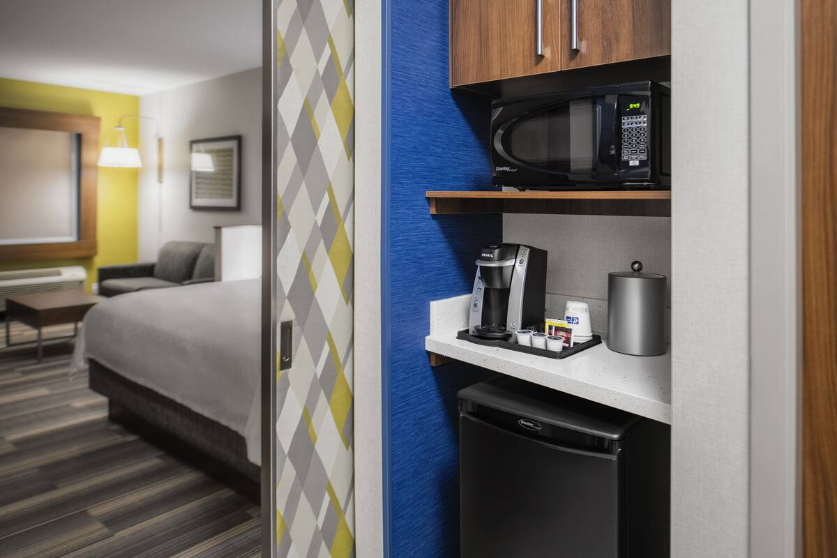 A hotel room with a bed, a desk, a microwave, a coffee maker, and a mini-fridge.