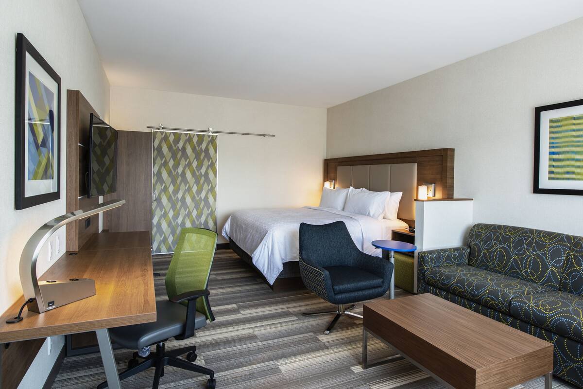 A hotel room with a bed, a desk with a chair, a sofa, and a TV on the wall.