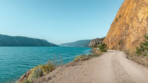 Ein Feldweg entlang eines Gewässers, mit einer felsigen Klippe an einer Seite.