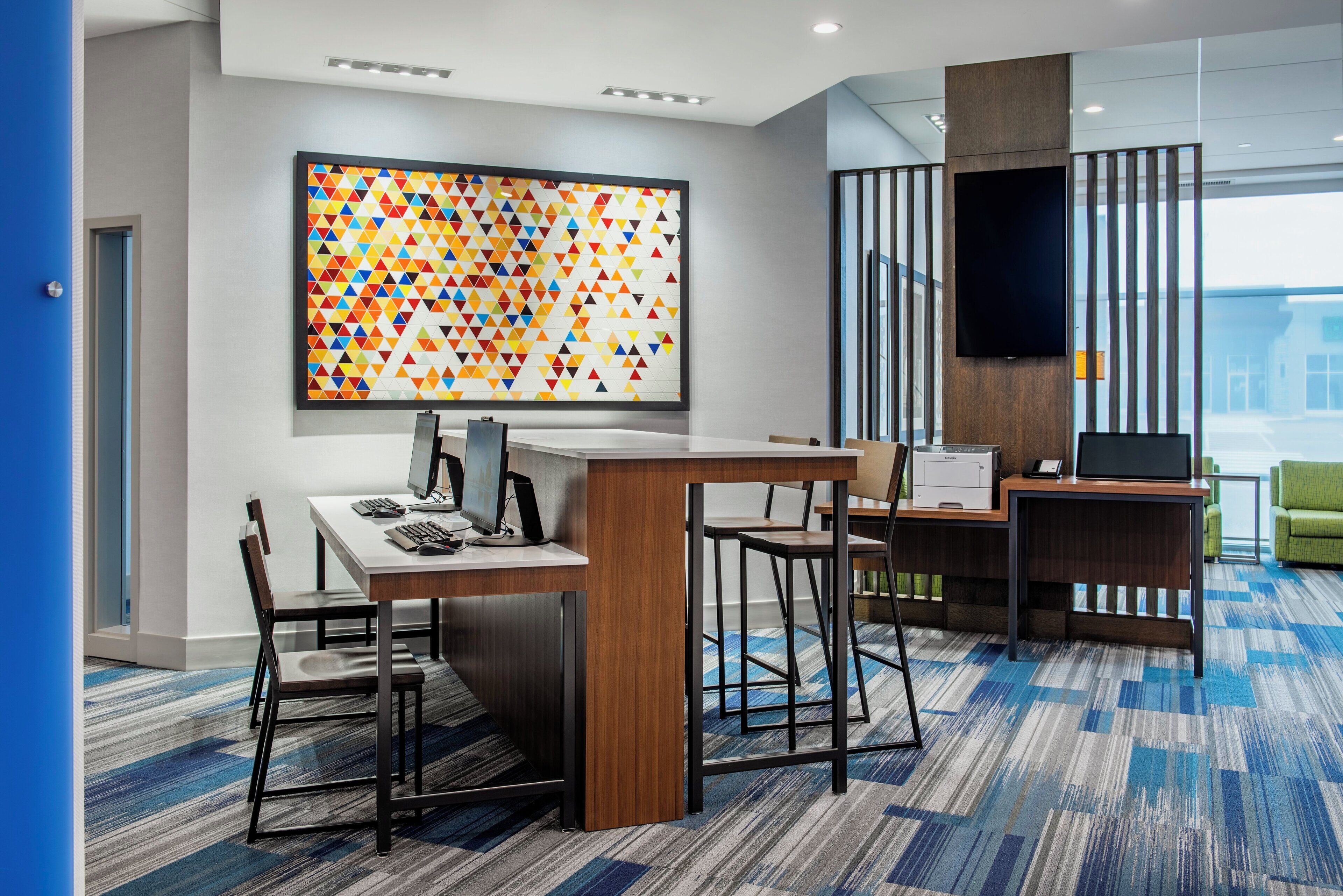 A modern office space with a large geometric artwork on the wall, a desk with a computer, and a television mounted on the wall.