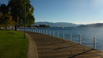 A wooden boardwalk along a waterfront with a clear view of the water and distant mountains.